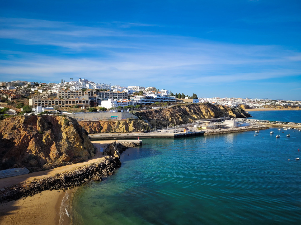 View across the sheltered waters of Albufeira Marina, with small boats, sandy coves and white buildings rising above the golden coastal cliffs.