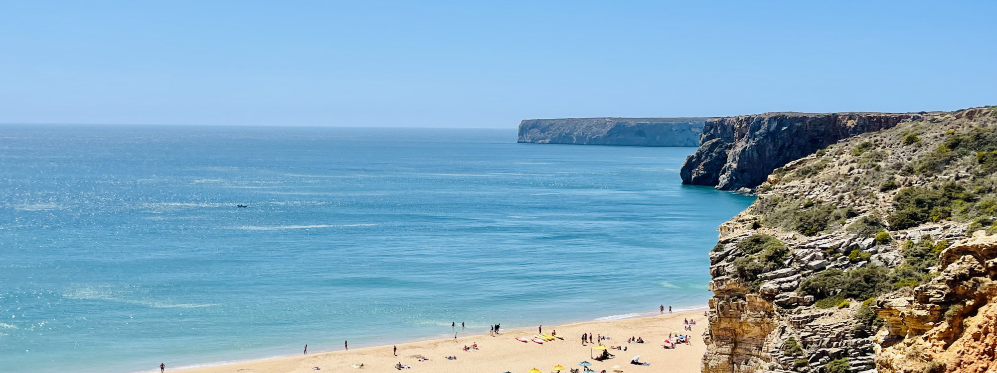 Praia do Beliche near Sagres in the Algarve, Portugal, seen from the surrounding coastal cliffs. The image shows a broad sandy beach, blue Atlantic waters and the rocky headlands of Portugal’s southwestern coast.