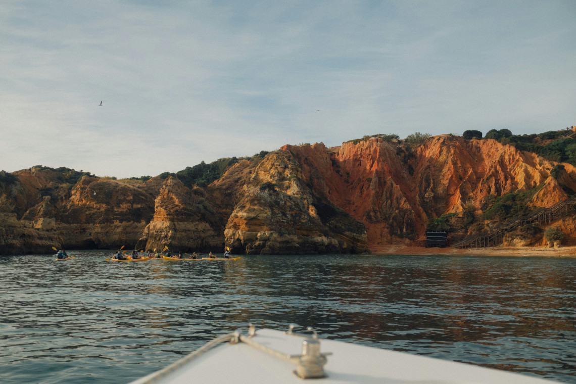 View from the water toward the golden and reddish cliffs of Ponta da Piedade, with kayakers exploring the sheltered coastline near Lagos.
