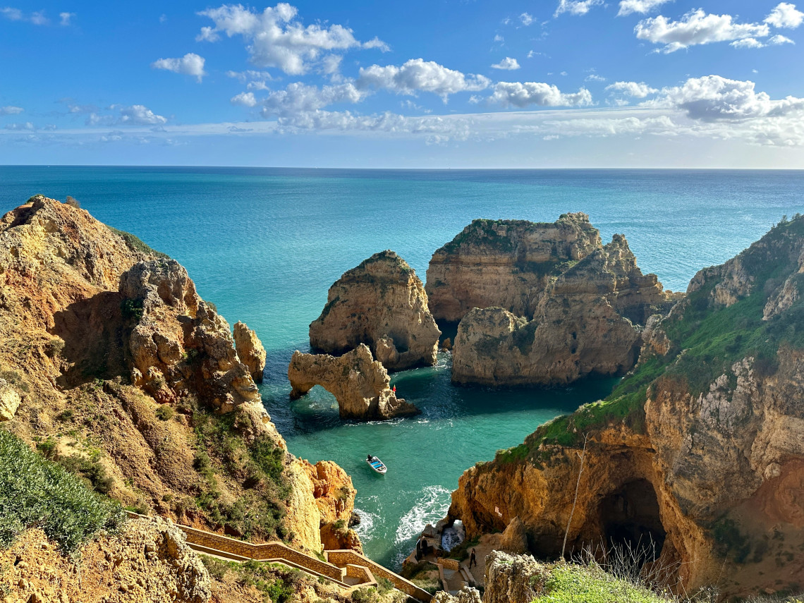 View from the cliffs of Ponta da Piedade in Lagos, overlooking turquoise Atlantic waters, sculpted limestone formations, sea arches and a small sightseeing boat.