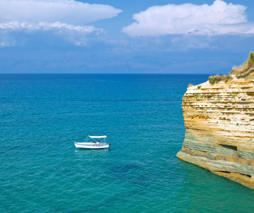 A sightseeing boat cruises beside layered golden limestone cliffs and clear blue Atlantic waters along the Lagoa coast in the Algarve.