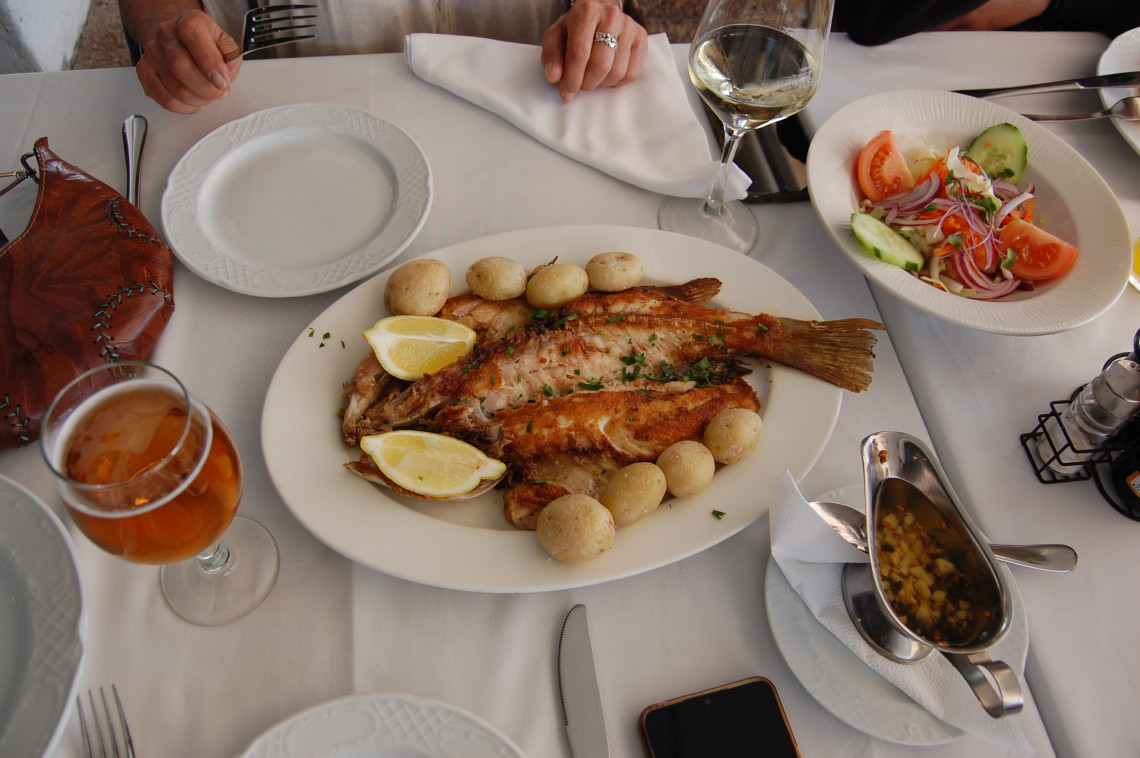 Whole grilled fish served with boiled potatoes, lemon wedges and fresh herbs at a restaurant in the Algarve, Portugal. A mixed salad and garlic dressing accompany the traditional Portuguese seafood meal.