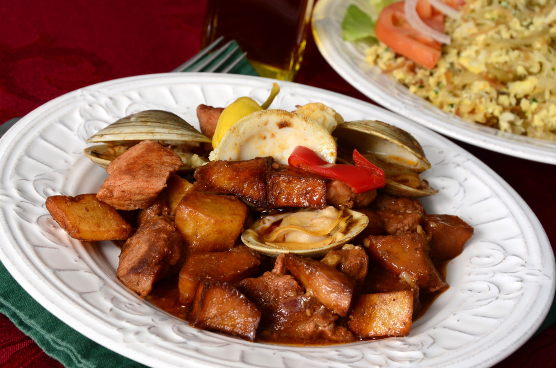 Carne de Porco &agrave; Alentejana served in the Algarve, Portugal, combining marinated pork, clams and fried potatoes in a seasoned sauce. The traditional Portuguese dish is garnished with pickled vegetables and lemon.