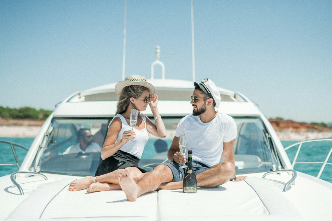 A couple sits on the deck of a private yacht in the Algarve, Portugal, sharing drinks while cruising along the coast. The image shows a relaxed boating experience surrounded by calm Atlantic waters.