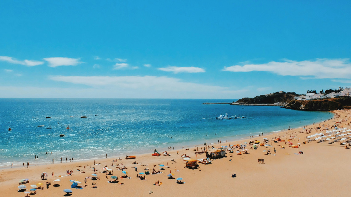 Wide view of Praia dos Pescadores in Albufeira, with visitors and beach umbrellas spread across the golden sand beside calm blue Atlantic waters.