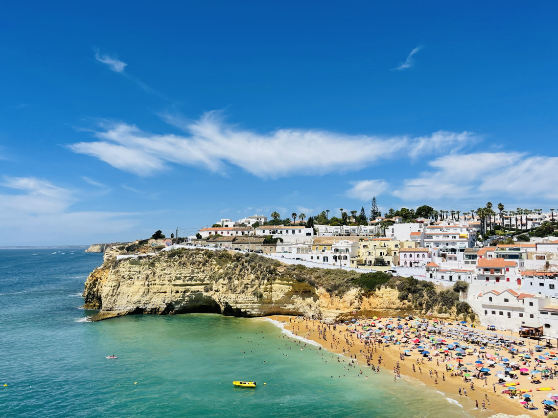 View over Praia do Carvoeiro in Lagoa, where a sandy cove with turquoise water is surrounded by golden cliffs and whitewashed buildings of the coastal village.