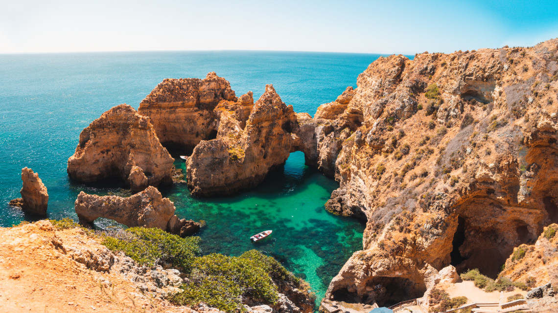 Elevated view of the limestone arches, caves and rock pillars at Ponta da Piedade in Lagos, Algarve, Portugal. A small boat moves through the clear turquoise water enclosed by the coastal formations.