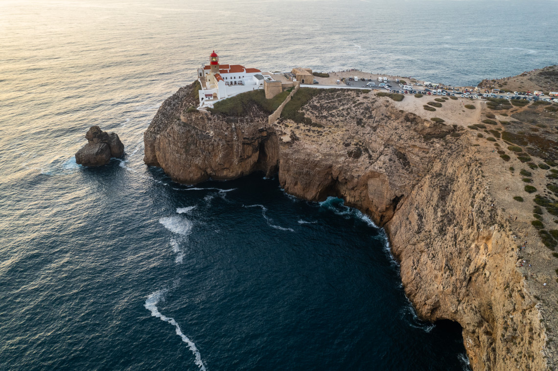 Aerial view of Cape St Vincent Lighthouse near Sagres in the Algarve, Portugal, standing above steep cliffs at the southwestern edge of the country. The rocky headland extends into the Atlantic Ocean, with waves breaking below the lighthouse complex.
