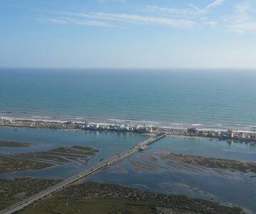 Aerial view of Praia da Ilha de Faro showing the narrow barrier island between the Atlantic Ocean and the Ria Formosa lagoon, connected to the mainland by a bridge.