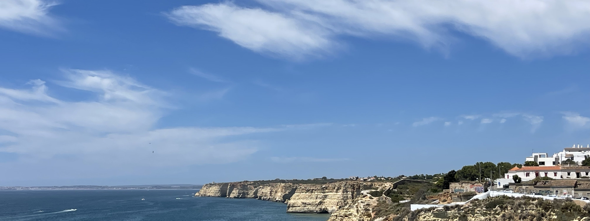 Panoramic view of the coastline in Carvoeiro, Algarve, Portugal, featuring whitewashed houses overlooking golden limestone cliffs and the Atlantic Ocean. The image showcases the dramatic coastal scenery that makes the Algarve one of Portugal's most popula