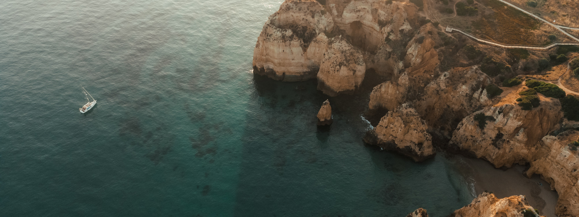 Panoramic view of the coastline in Carvoeiro, Algarve, Portugal, featuring whitewashed houses overlooking golden limestone cliffs and the Atlantic Ocean. The image showcases the dramatic coastal scenery that makes the Algarve one of Portugal's most popula