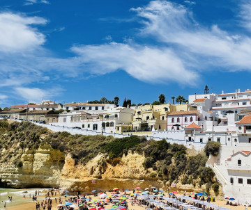 View of Praia do Peneco in Albufeira, Algarve, Portugal, featuring golden sandstone cliffs, a sandy beach, and the whitewashed buildings of Albufeira's historic center overlooking the Atlantic coastline.
