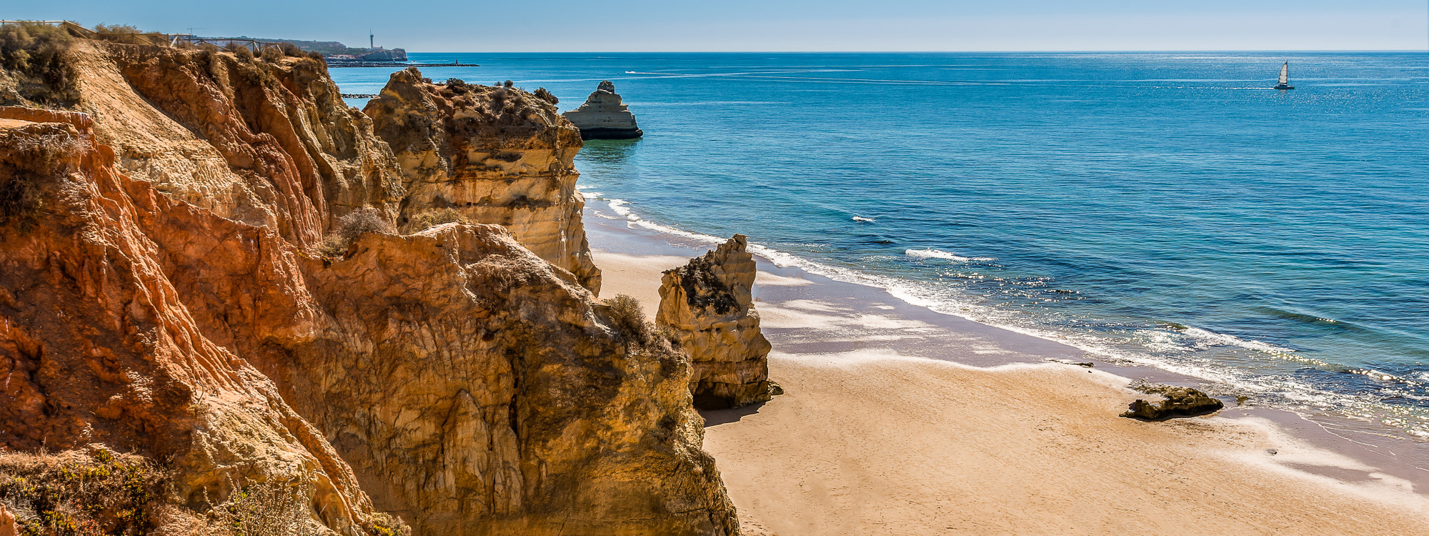 View of Praia dos Três Castelos in Portimão, Algarve, Portugal, featuring golden limestone cliffs, a sandy beach, and the Atlantic Ocean. The coastline is known for its rugged rock formations, scenic viewpoints, and dramatic seaside landscapes along Portu