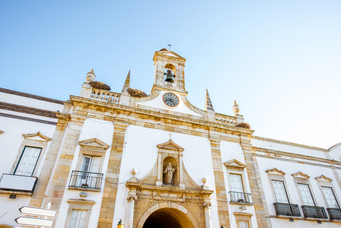 Arco da Vila in Faro, Algarve, Portugal, featuring its neoclassical fa&ccedil;ade, bell tower, and historic archway leading into the city's old town. The monument is one of Faro's most recognizable landmarks and a key attraction in the Algarve region.
