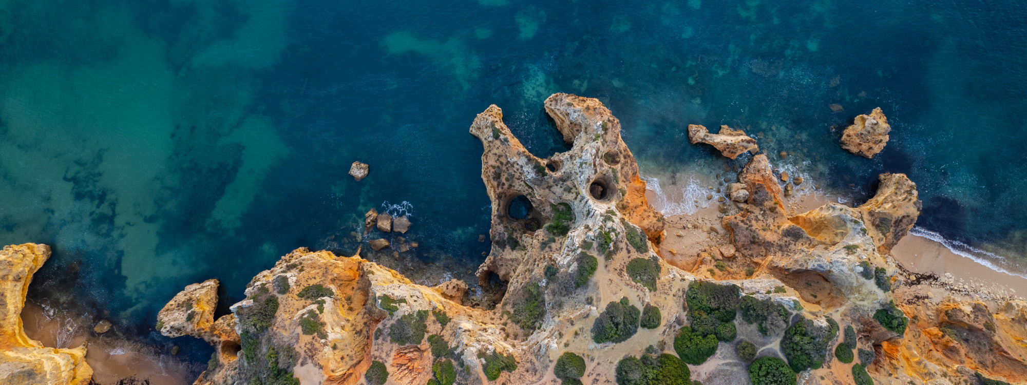 Aerial view of Ponta da Piedade in Lagos, Algarve, Portugal, showcasing golden limestone cliffs, sea arches, rocky outcrops, and turquoise Atlantic waters. The image highlights one of the Algarve's most iconic coastal landscapes, shaped by centuries of er