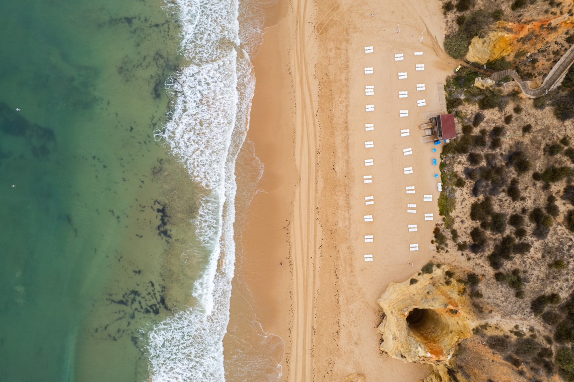 Top-down aerial view of Praia da Rocha in Portim&atilde;o, Algarve, Portugal, showing golden sand, Atlantic waves, sun loungers, and the distinctive limestone cliffs that line the coastline. The image highlights one of the Algarve's most iconic beach destinations from above.
