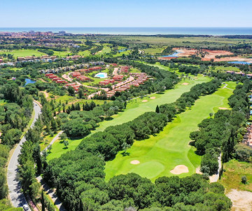Aerial view of a landscaped golf course in the Algarve, with long green fairways, sand bunkers, pine trees and resort developments extending toward the coast.