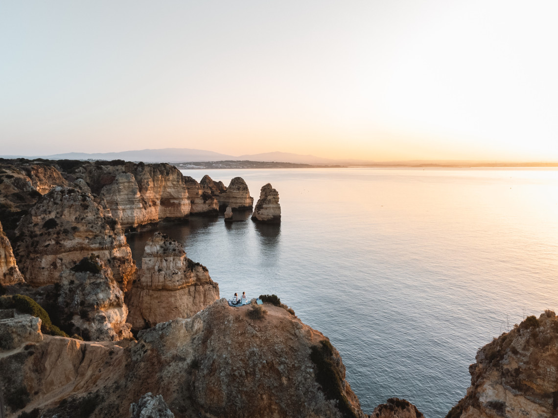 Dramatic golden limestone cliffs and towering rock stacks at sunset overlooking the Atlantic Ocean in the Portuguese Algarve, with golden hour light reflecting on calm waters